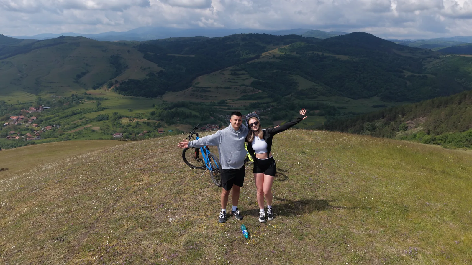 A couple on a hilltop with a bike, panorama over the Apuseni